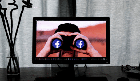 Homem na tela do computador olhando através de um binóculo com logotipo do facebook